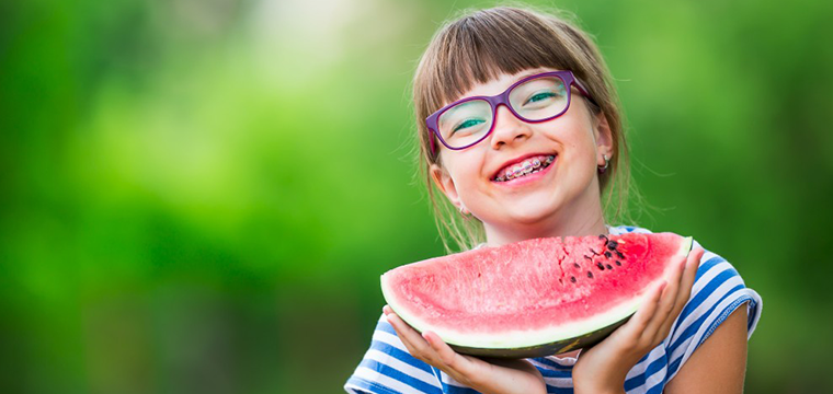 Manhattan Bridge Orthodontics Smiling girl with glasses holding a watermelon